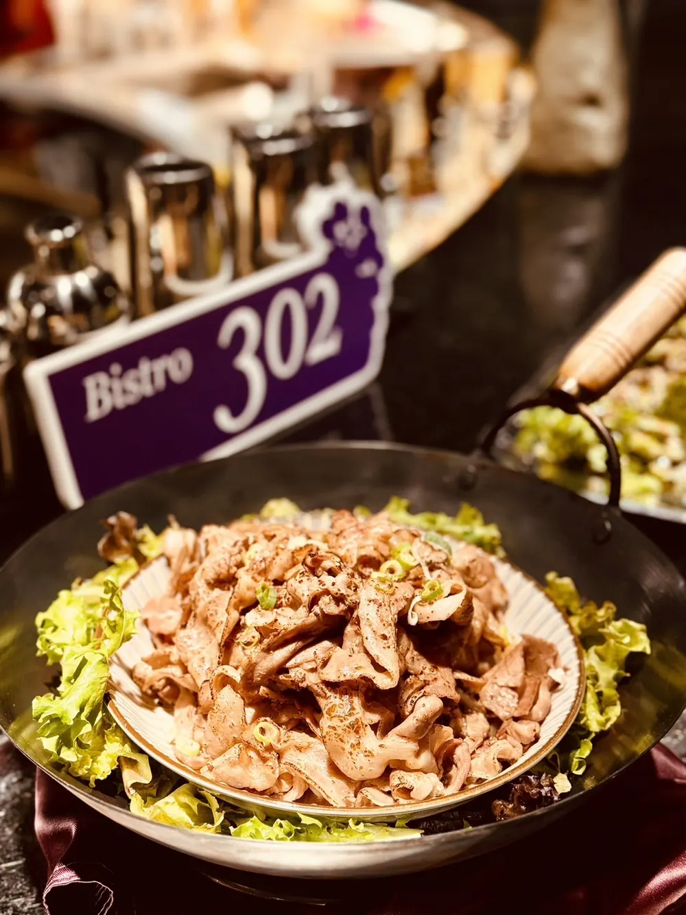一盤炒肉片沙拉，旁邊立著紫色的 Bistro 302 桌牌