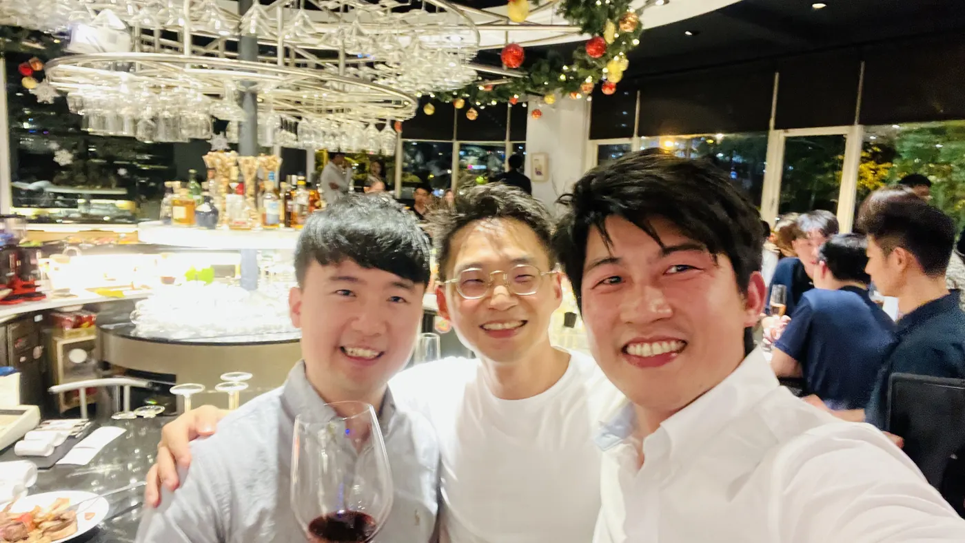 三位與會者在吧台前自拍，其中一位拿著紅酒杯