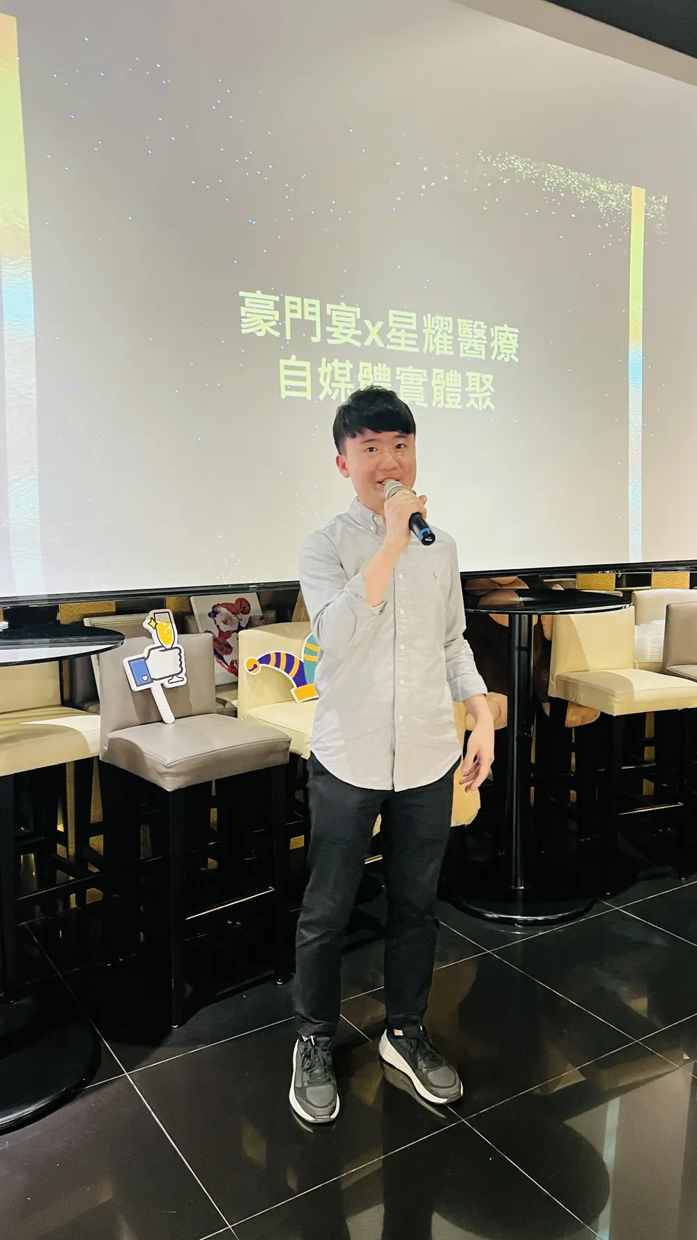 一位穿淺灰色襯衫的與會者手持麥克風站在投影幕前
