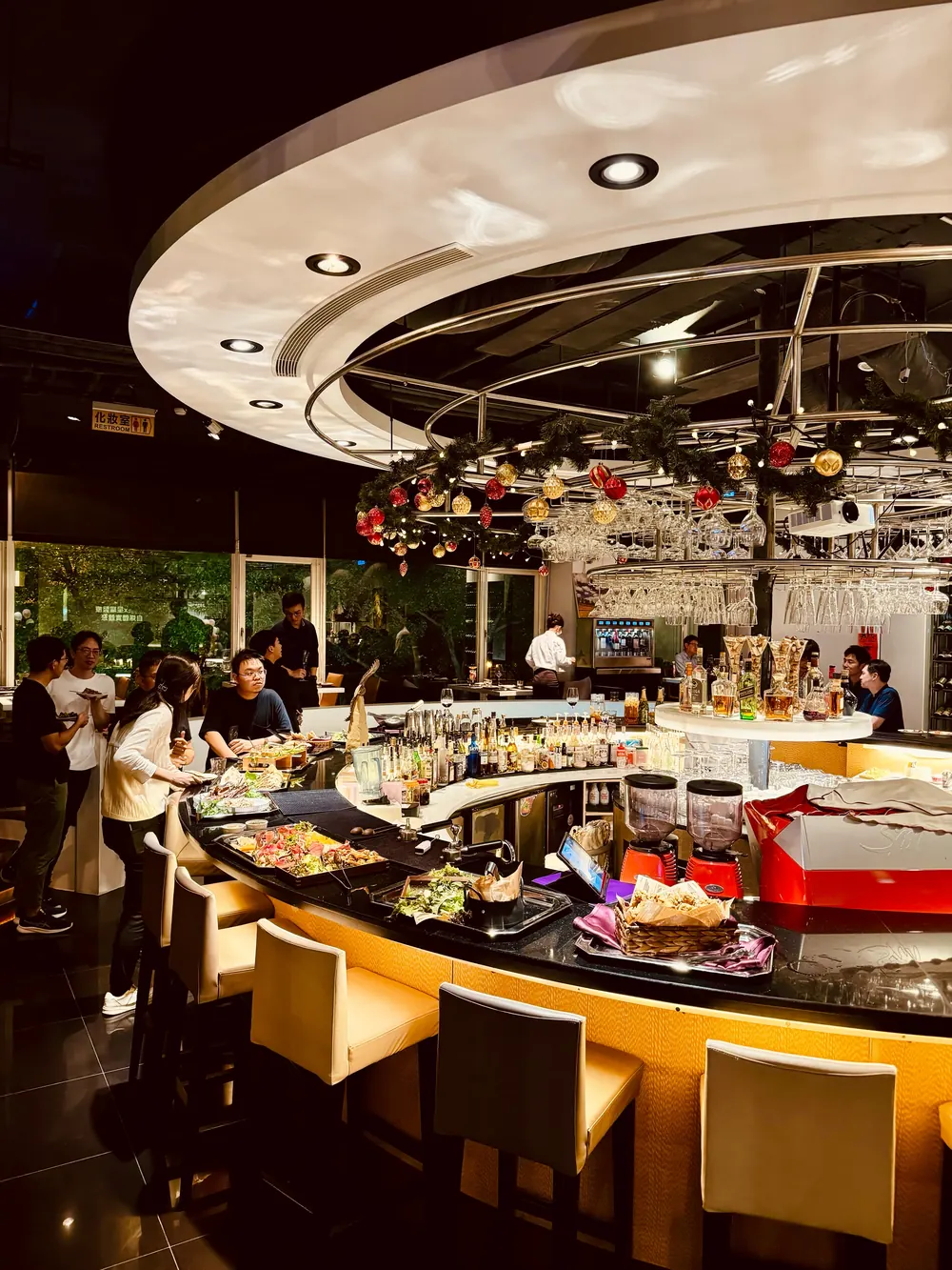 圓形吧台上擺滿餐點與酒杯，天花板掛著聖誕綠圈裝飾