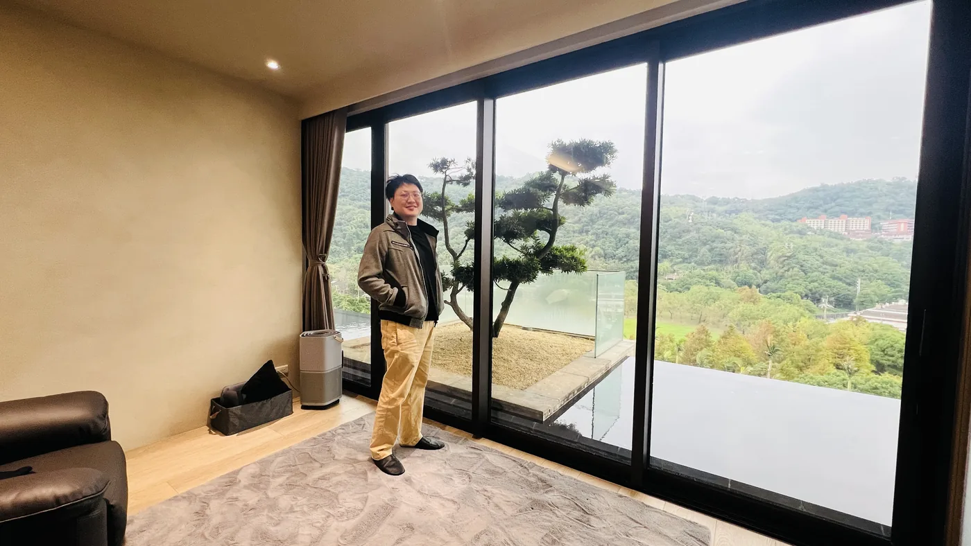一位與會者站在原蘊醫學診所的落地窗前，窗外是士林的山景與綠地