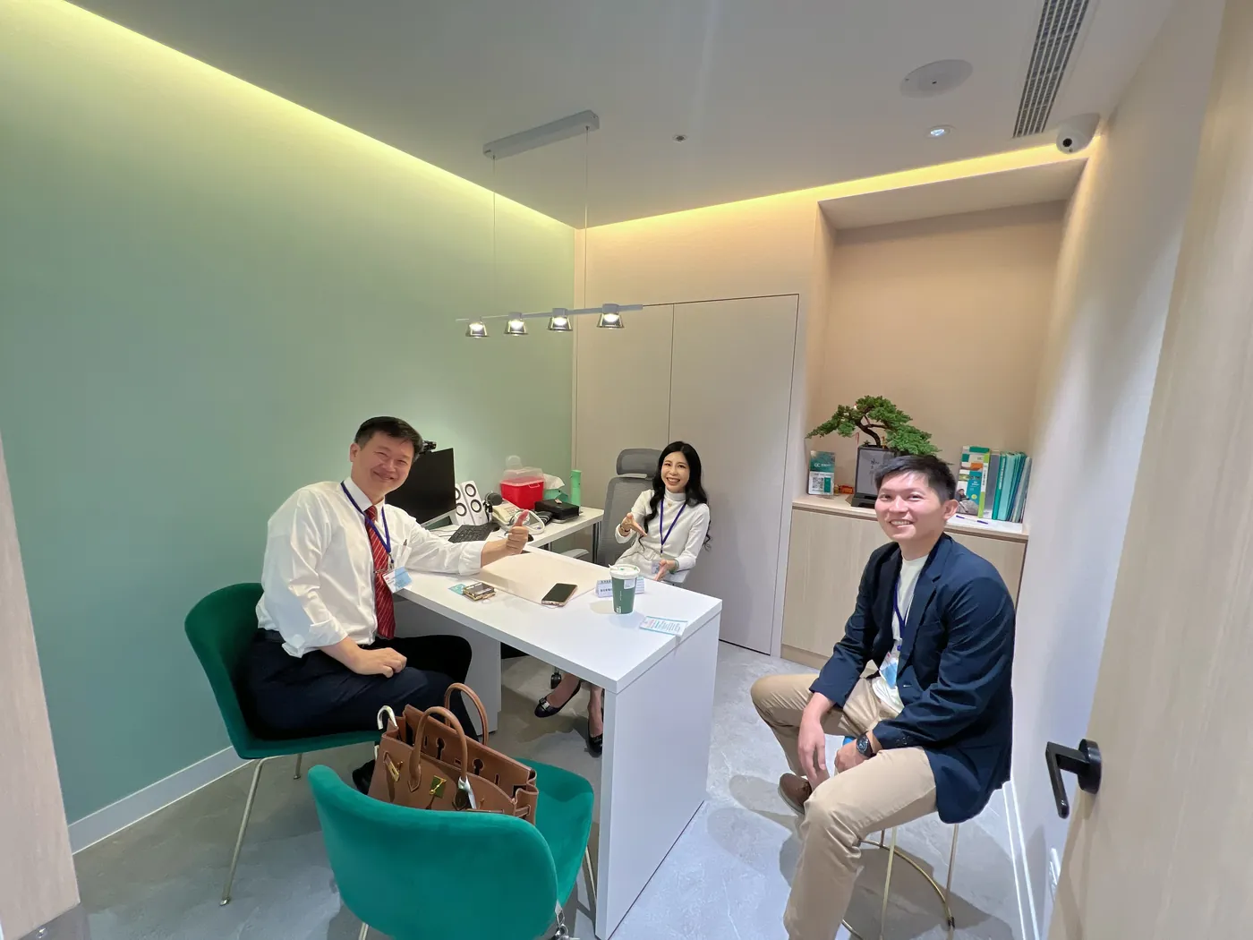 三位與會者坐在康博診所一間湖水綠牆面的診間裡，笑著看向鏡頭