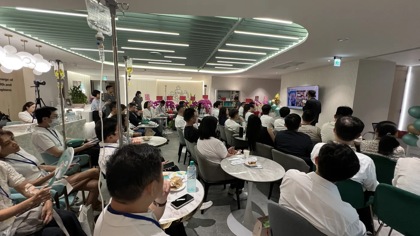 康博診所大廳內，與會醫師坐滿圓桌與沙發，面向前方的螢幕聽講