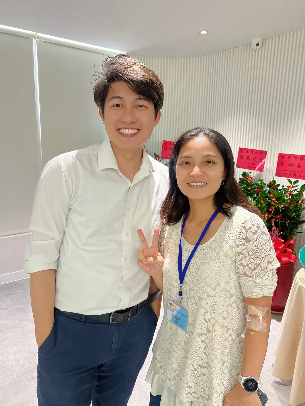 張益豪醫師與一位掛著名牌的女醫師在花籃旁合影，對方比出 YA