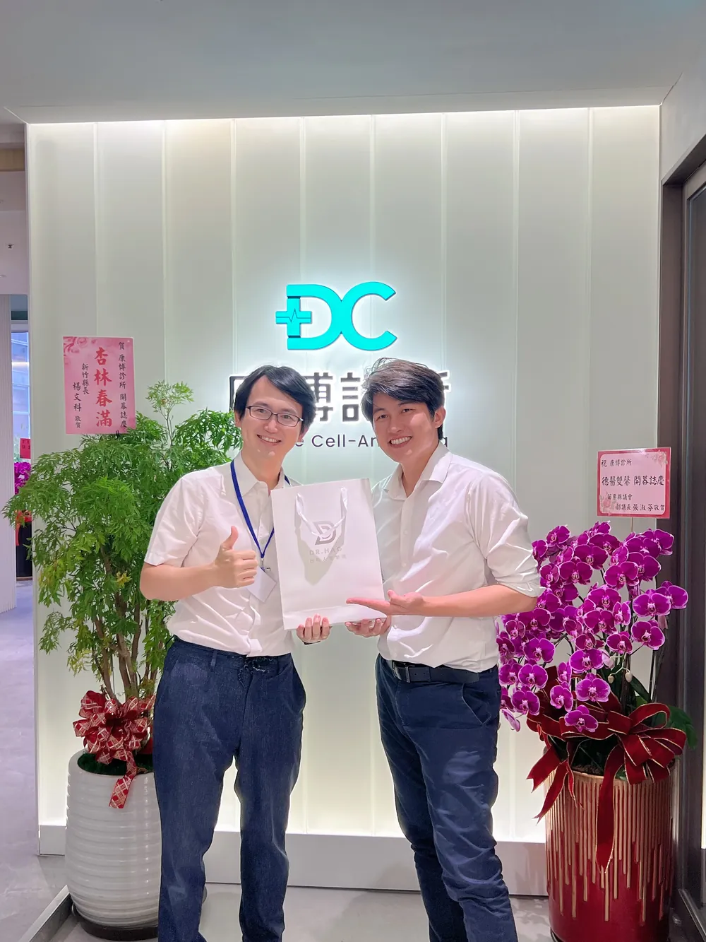 張益豪醫師與謝東穎醫師在招牌前比讚，手上拿著伴手禮袋