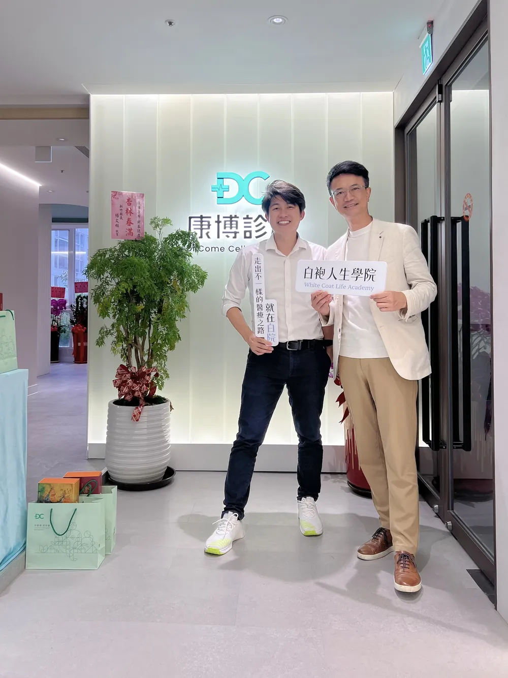同一組人在招牌前退後幾步的全身照，手上舉著白袍人生學院立牌