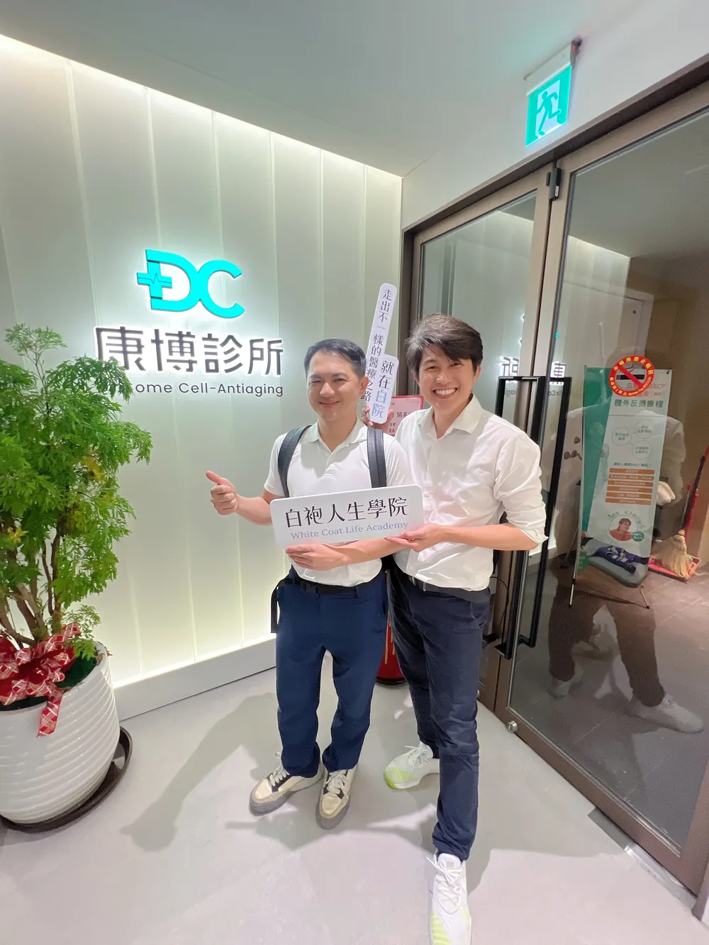 胡守丞醫師與張益豪醫師在招牌前，舉著白袍人生學院立牌