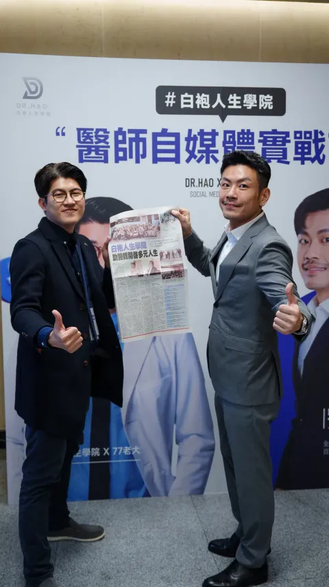 張益豪醫師與 77 老大在活動背板前合影，手持刊有白袍人生學院報導的經濟日報