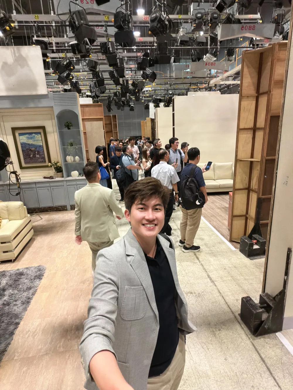 張益豪醫師在另一組客廳佈景前自拍，後方參訪醫師正在參觀