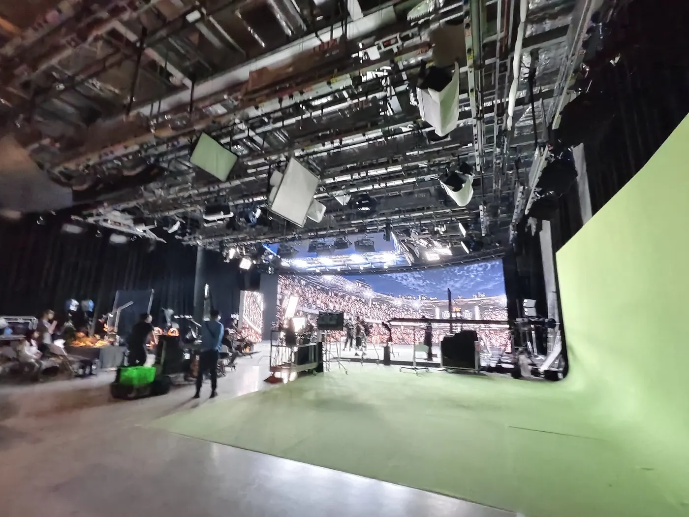大型攝影棚全景，左側是顯示球場觀眾席畫面的 LED 牆，右側是綠幕，上方是密集的燈架